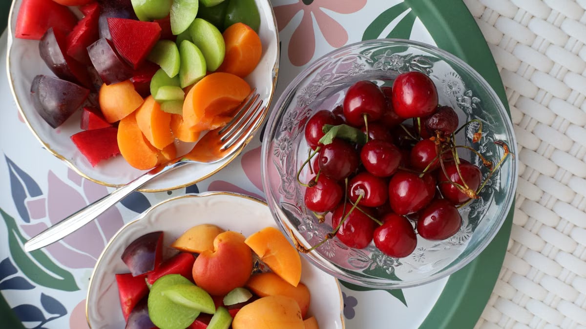 Vibrant mix of fresh summer fruits in decorative bowls on a floral patterned tray.