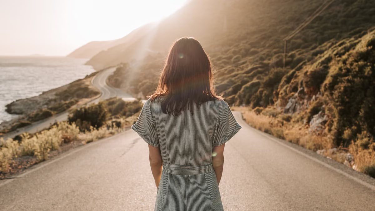 A woman stands on a coastal road in Antalya, Turkey, admiring the sunset.